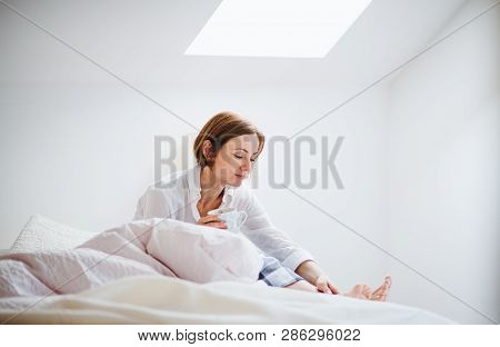 A Young Woman With Night Shirt Sitting Indoors On Bed In The Morning, Holding Cup.