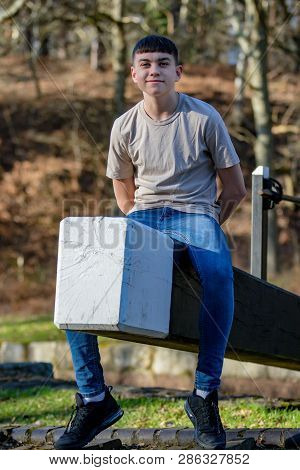 Portrait Of A Caucasian Teenage Boy On A Warm Spring Day Sitting On A Lock Gate