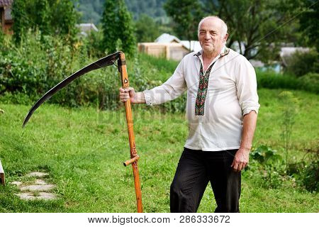 Hutsul From Carpathian Mountains. Hutsul In Traditional Dress Standing With Scythe Outdoors. Nationa