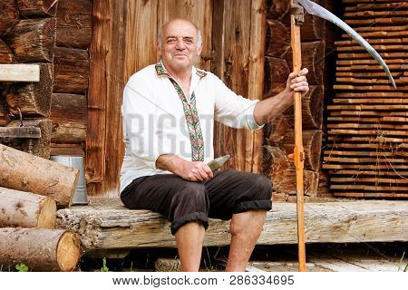 Man In Embroidered Shirt With Scythe. Portrait Of Senior Hutsul Man Outdoors. Traditions Of The Carp