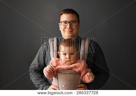 Fathre And His Kid In Baby Carrier At The Grey Background Wall, Baby Wearing Concept