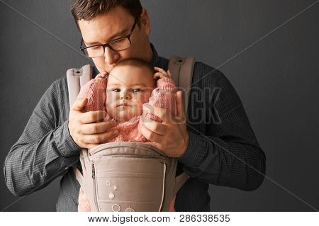 Fathre And His Kid In Baby Carrier At The Grey Background Wall, Baby Wearing Concept