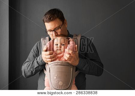 Fathre And His Kid In Baby Carrier At The Grey Background Wall, Baby Wearing Concept