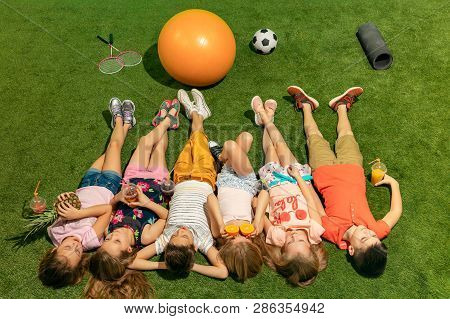 Group Of Happy Children Playing Outdoors. Kids Having Fun In Spring Park. Friends Lying On Green Gra