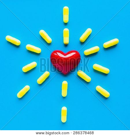 Yellow Pills Around A Red Heart Fell From A Bottle On A Blue Background. Flat Lay, Top View.