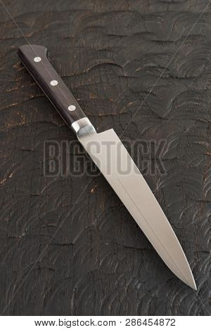 Small kitchen knife on dark wooden cutting board