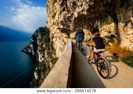 Cycling woman and man riding on bikes at sunrise mountains and Garda lake landscape. Couple cycling MTB enduro flow sentiero ponale trail track. Outdoor sport activity.