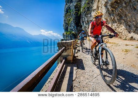 Cycling woman and man riding on bikes at sunrise mountains and Garda lake landscape. Couple cycling MTB enduro flow sentiero ponale trail track. Outdoor sport activity.