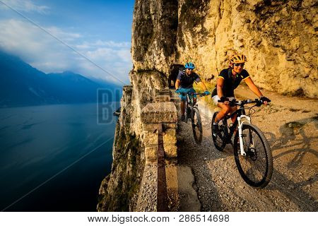 Cycling woman and man riding on bikes at sunrise mountains and Garda lake landscape. Couple cycling MTB enduro flow sentiero ponale trail track. Outdoor sport activity.
