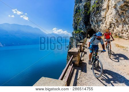 Cycling woman and man riding on bikes at sunrise mountains and Garda lake landscape. Couple cycling MTB enduro flow sentiero ponale trail track. Outdoor sport activity.
