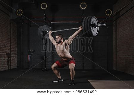 Young fit athlete lifting heavy barbell overhead at the gym. Handsome man doing functional trai