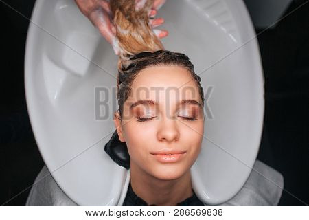 Top View Of Beautiful Young Woman With Closed Eyes Smiling While Hairdresser Washing Blonde Hair. Ha