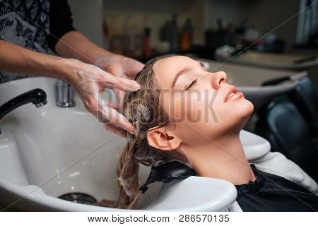 Beautiful Young Woman Sitting Near Sink While Hairdresser Washing Her Hair In Beauty Salon. Hair Sty