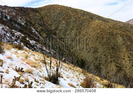 Arid Landscape Including Barren Mountains Covered In Snow With Burnt Chaparral Shrubs Caused From A 