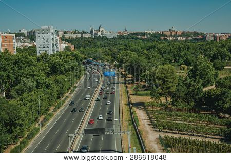Multi-lane Highway With Heavy Traffic In The Midst Of Garden Trees And Apartment Buildings, In A Sun