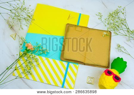 Top View Vintage Book With Empty Sheets,brigt Paper Folder,squishy Toy Pineapple  And Flowers On A M