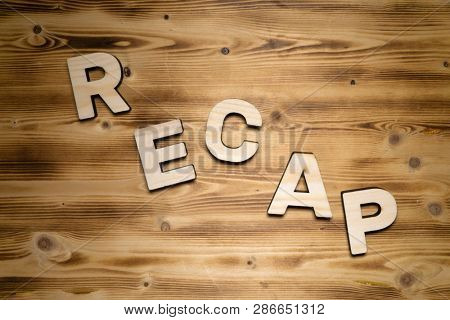 RECAP word made of wooden block letters on wooden board.