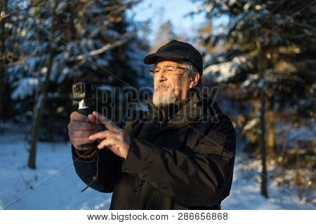 Handsome senior man shotting video with his adventura outdoor camera on a grip handle outdoors on a lovely winter day, enjoying retirement
