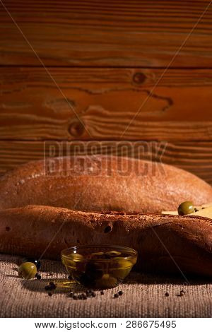 Fresh Bread Baguette With Olive Oil, Olives. Cheese And Rosemary On Wooden Background. Teasty Breakf