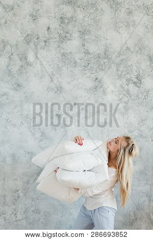 Pillow Comfort. Young Satisfied Blonde Woman Holding Pile Of Pillows. Copy Space On Grey Textured Ba