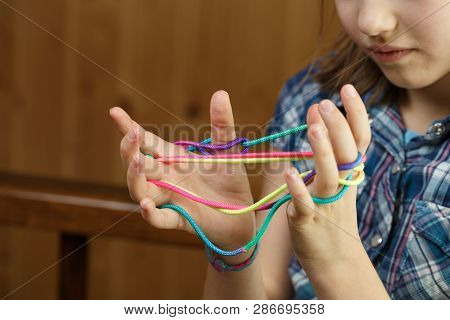 Child Playing Classic, Old-school String Game And Didactic Toy With Her Fingers, Making Cats Cradle,
