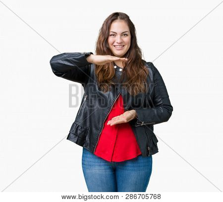 Beautiful plus size young woman wearing a fashion leather jacket over isolated background gesturing with hands showing big and large size sign, measure symbol. Smiling looking at the camera. Measuring