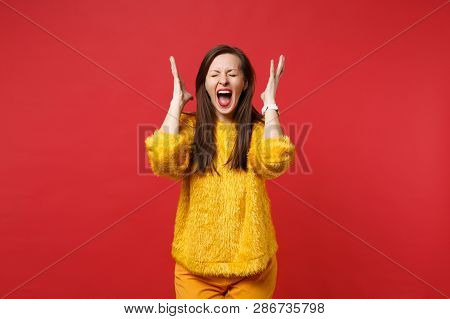 Portrait Of Crazy Young Woman In Yellow Fur Sweater With Closed Eyes Screaming Rising Hands Isolated