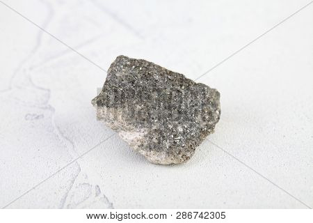 Natural Mineral Rock Specimen - Raw Arsenopyrite Stone On White Cement Background From Kachkarskoe, 