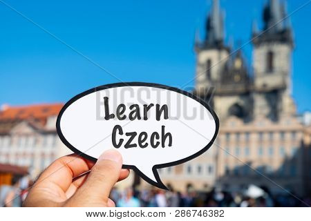 closeup of the hand of a young caucasian man showing a speech bubble with the text learn Czech written in it, on the Old Town Square in Prague, Czech Republic