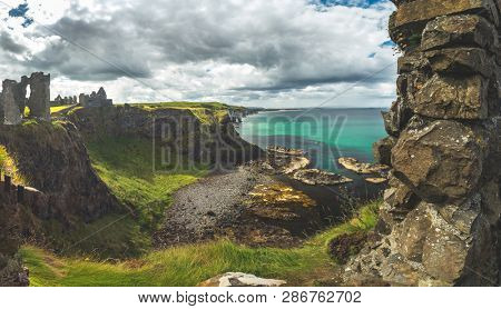 The overview from Dunluce castle to the Irish bay. Overwhelming Northern Ireland landscape. Epic shoreline view from above the cliff. The ruins of the Medieval building under the cloudy rainy sky.