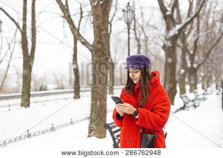 Image of a beautiful young woman using mobile phone walking outdoors in snow winter.