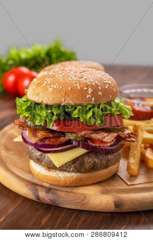Hamburgers with fried bacon and sliced pickles  on a cutting board with french fries and tomato sauce
