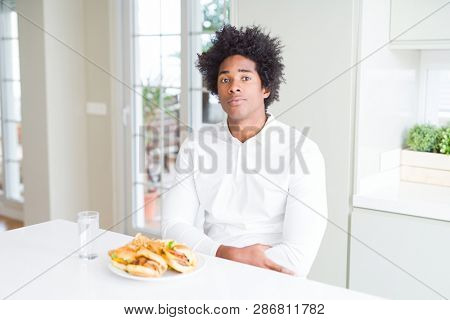 African American hungry man eating hamburger for lunch with serious expression on face. Simple and natural looking at the camera.