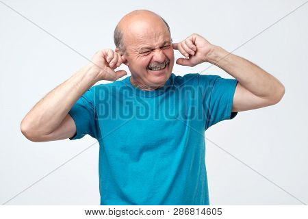 Senior Hispanic Bald Guy Plugging Ears With Fingers Hearing Loud Sounds Of Music