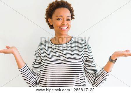 Young beautiful african american woman wearing stripes sweater over white background Smiling showing both hands open palms, presenting and advertising comparison and balance