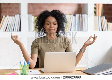 Calm Black Businesswoman Taking Break Meditating Doing Yoga At Work