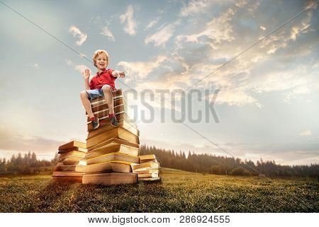 Little Boy Sitting On The Tower Made Of Big Books. Childhood Dreams, Reading And Education Concept. 