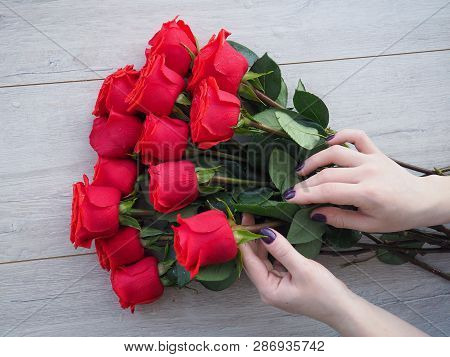 Preparing A Gift, On A Wooden Table, With Roses. Female Hand Holding A Gift, Wrapped With Ribbon, On