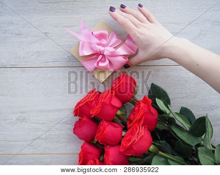 Preparing A Gift, On A Wooden Table, With Roses. Female Hand Holding A Gift, Wrapped With Ribbon, On