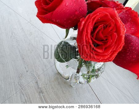 Preparing A Gift, On A Wooden Table, With Roses. Female Hand Holding A Gift, Wrapped With Ribbon, On