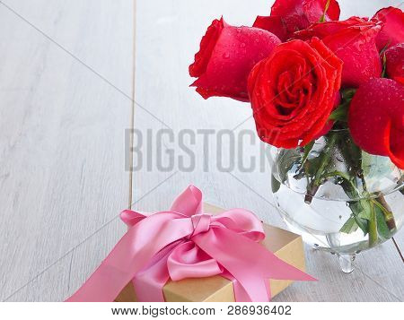Preparing A Gift, On A Wooden Table, With Roses. Female Hand Holding A Gift, Wrapped With Ribbon, On