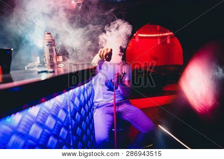 Man Smokes A Hookah And Breathes A Large Cloud Of Tobacco Smoke