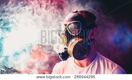 Man In A Gas Mask Smokes A Hookah And Breathes A Cloud Of Tobacco Smoke
