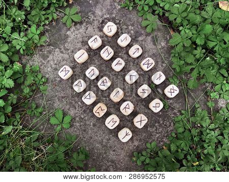 A Stack Of Wooden Runes At Forest. Wooden Runes Lie On A Rock Background In The Green Grass. Runes A