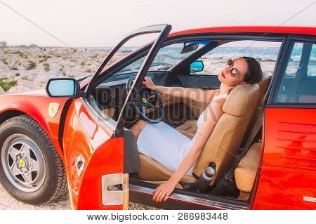 Young Girl In White Dress Sitting On The Front Seat Of The Red Ferrari