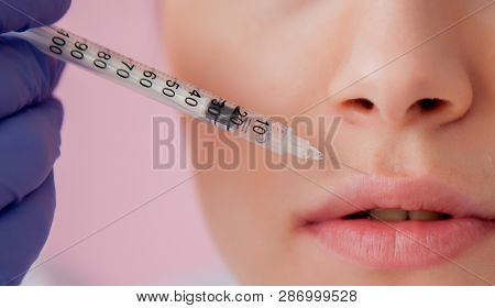 Doctor In Gloves Giving Woman Botox Injections In Lips, On Pink Background