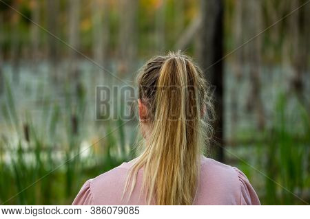 Young Caucasian Woman Standing Back To Camera In Evening Swamp With Blurred Dry Trees And Cattai In 