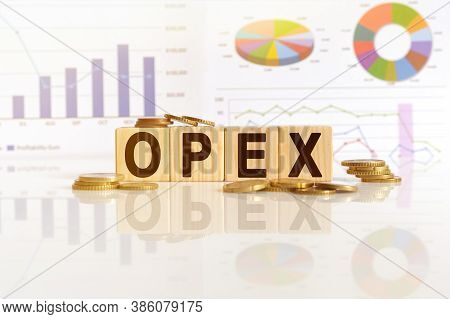 Opex The Word On Wooden Cubes, Cubes Stand On A Reflective Surface, In The Background Is A Business 