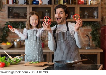Fun With Dad. Pretty Little Girl Playing With Father In Kitchen, Fooling With Bell Pepper Slices, Co