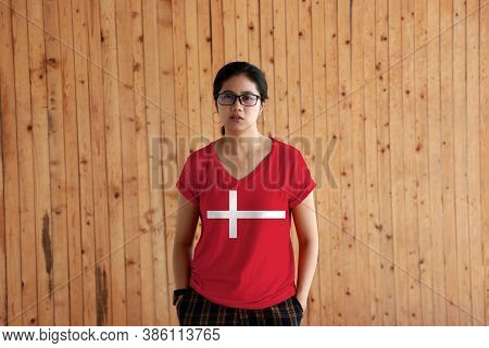 Woman Wearing Denmark Flag Color Shirt And Standing With Two Hands In Pant Pockets On The Wooden Wal
